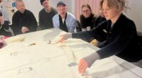kvinna vecklar ut en duk på ett bord och folk tittar på när hon berättar