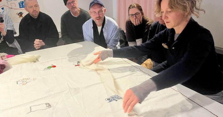 kvinna vecklar ut en duk på ett bord och folk tittar på när hon berättar