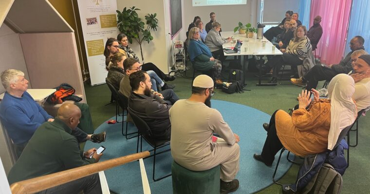 Människor som sitter i en stor ring runt ett långbord.