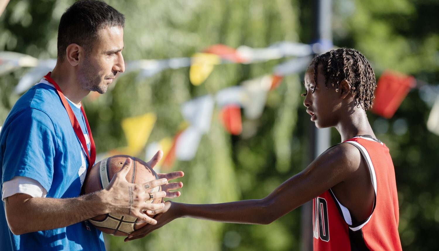 en man håller i en basketboll och en ung spelare försöker ta den
