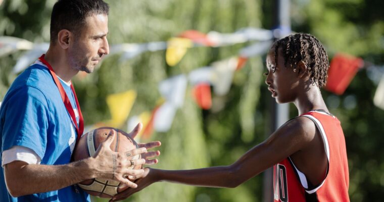 en man håller i en basketboll och en ung spelare försöker ta den