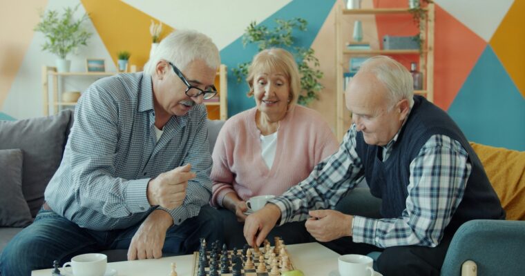 Tre seniorer, en kvinna och två män, spelar schack.