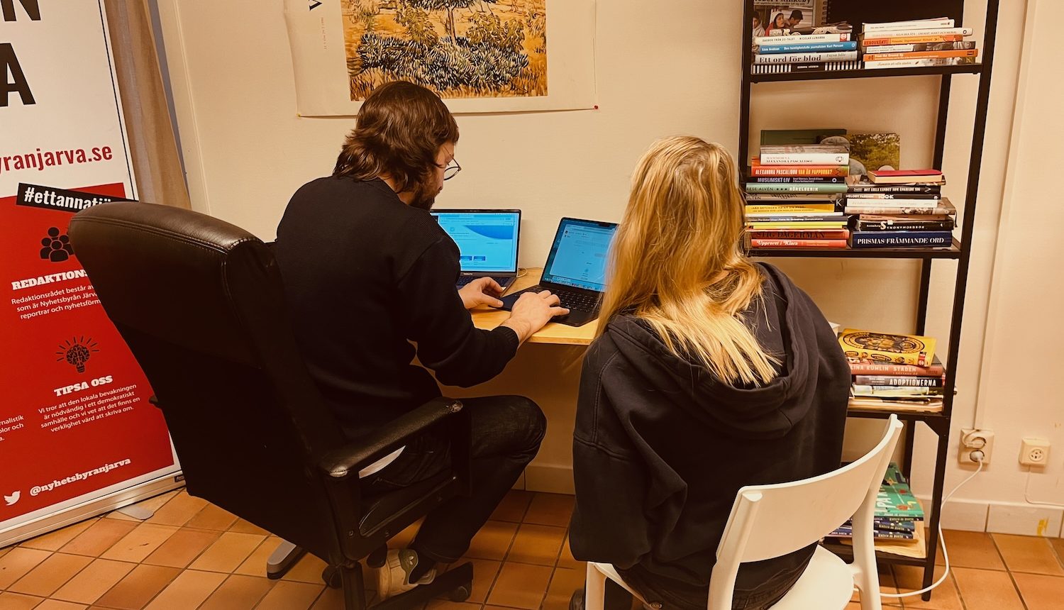 Två personer, en man och en kvinna, framför en dator vid ett bor på redaktionen.