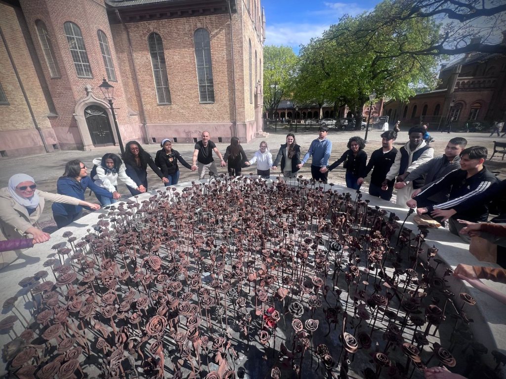 Eleverna står runt ett konstverk med rosor i metall, järnrosorna utanför Oslo domkyrka, ett minnesmonument efter terrorattackerna den 22 juli 2011.