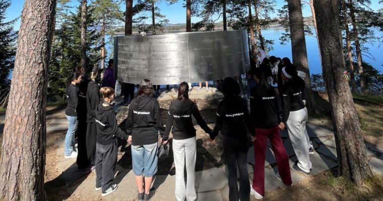 ungdomar står hand i hand i ring runt ett minnesmonument för de som dödades på Utøya