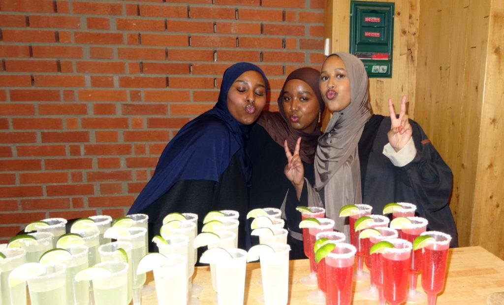 tre tjejer poserar bakom ett bord med drinkar