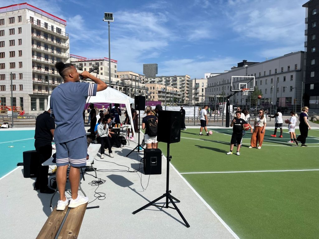en man rappar från en bänk framför en stadsvy med basketplaner