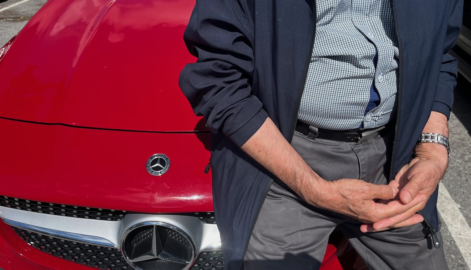 En äldre man sitter på huven till röda Mercedes Benz.