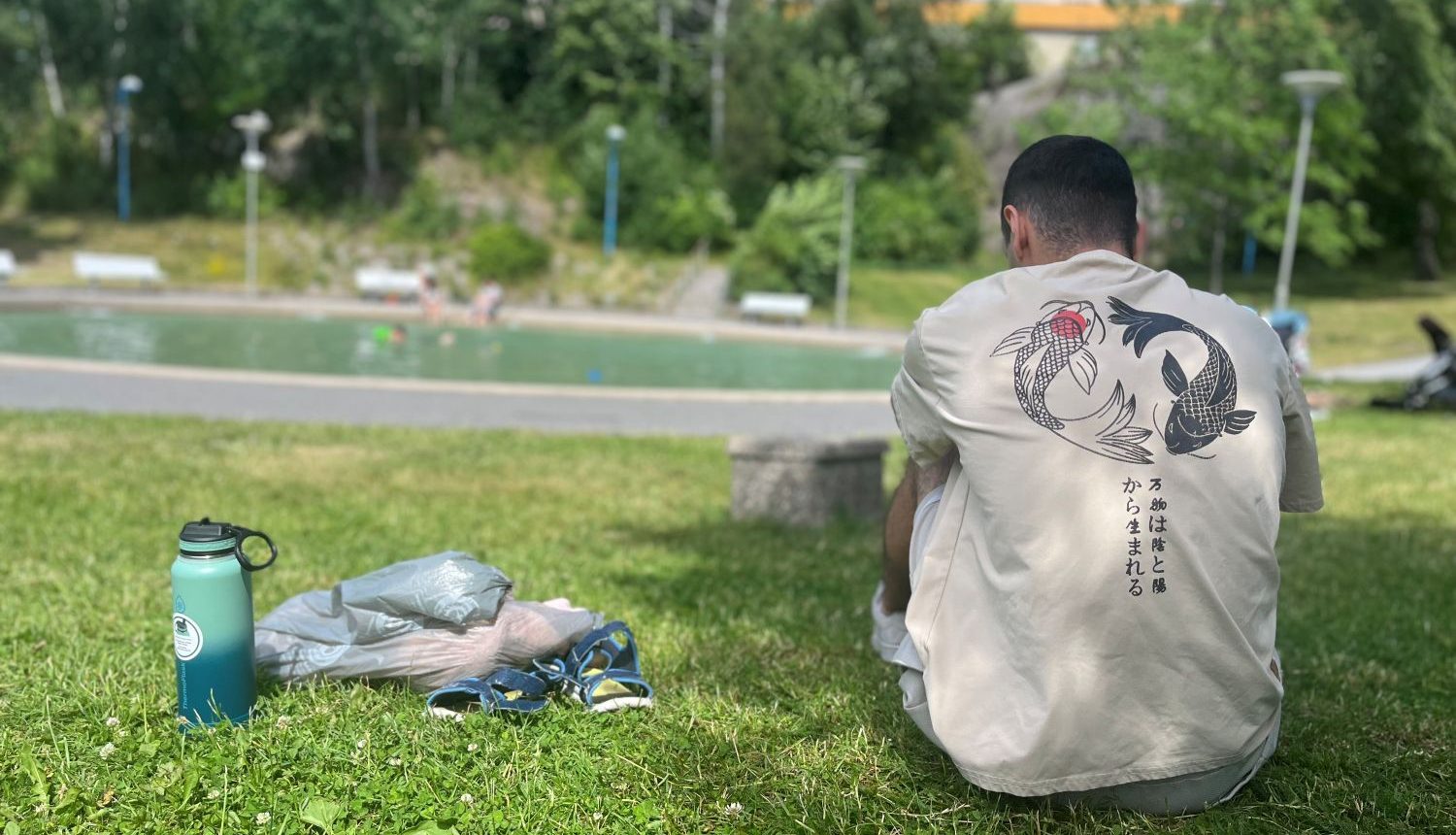 en man svalkar sig i skuggan under ett träd framför en plaskdamm