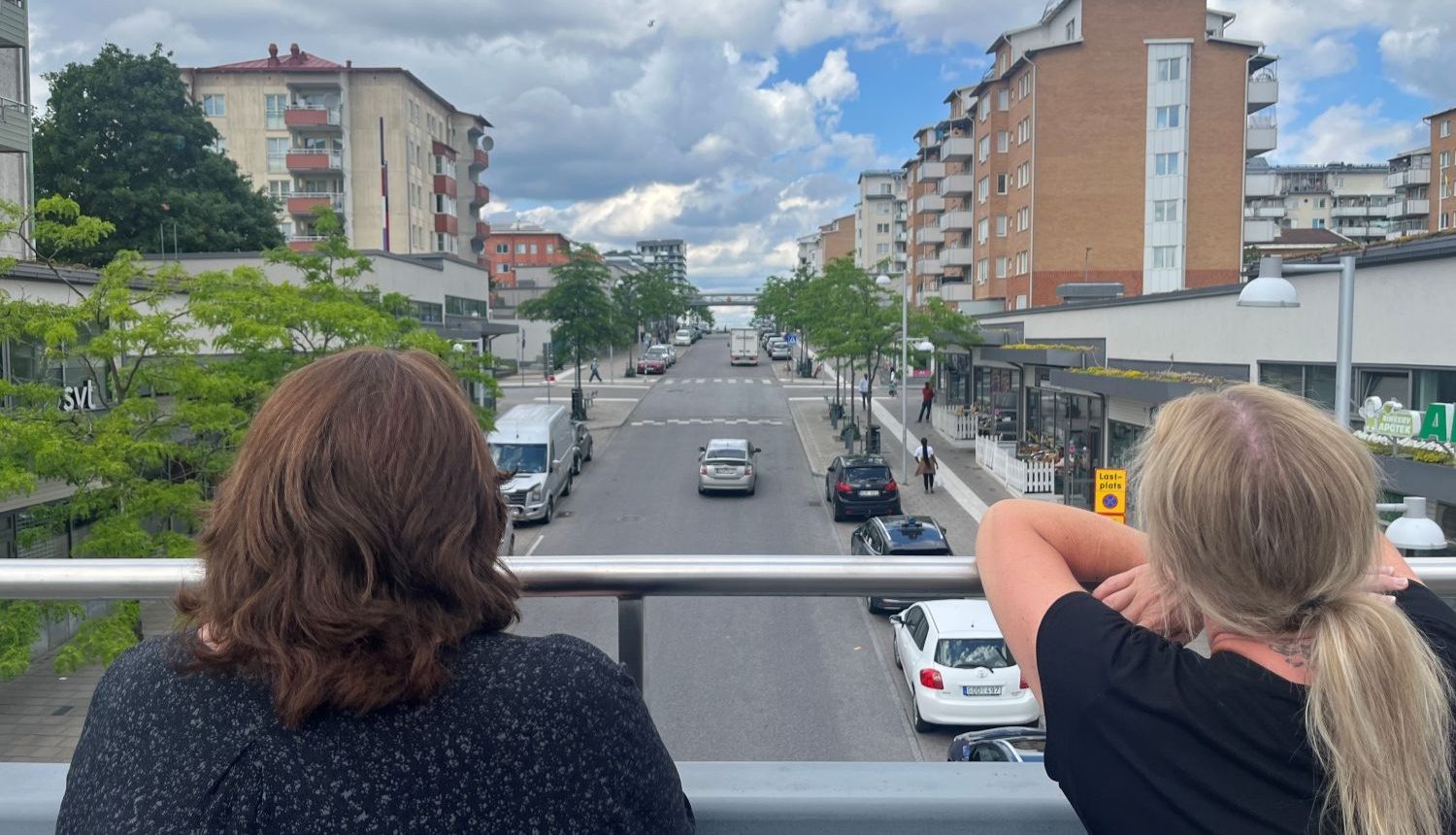 två kvinnor ser ut över en gata från en gångbro