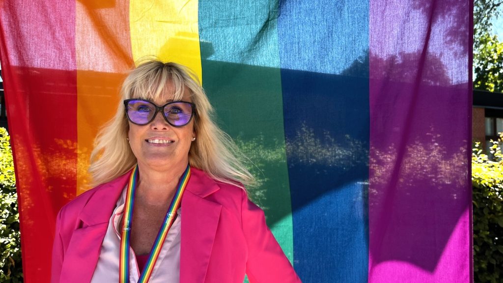 Blond kvinna framför Prideflaggan.