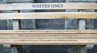 En parkbänk med orden Whites only målat på.