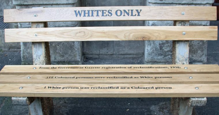En parkbänk med orden Whites only målat på.