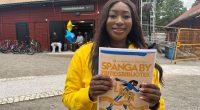 Kvinna ler mot kameran med en broschyr för Spånga by fritidsbibliotek framför sig