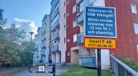 vägskyltar och bom framför höghus med bostadsrätter