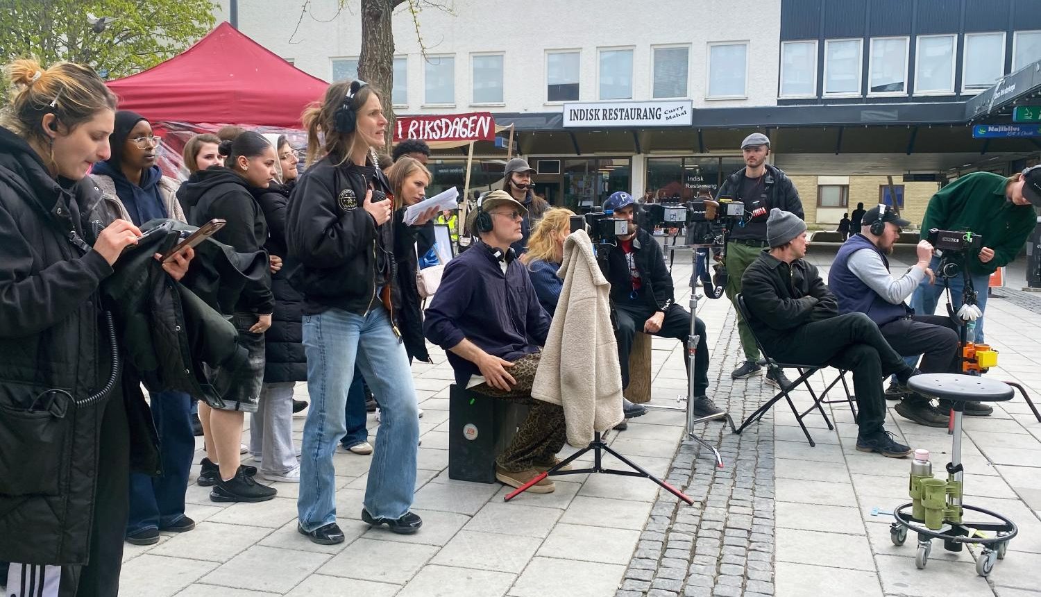 Kamerorna är riktade mot ingången till Rinkeby torg när dagens sista scen spelas in.