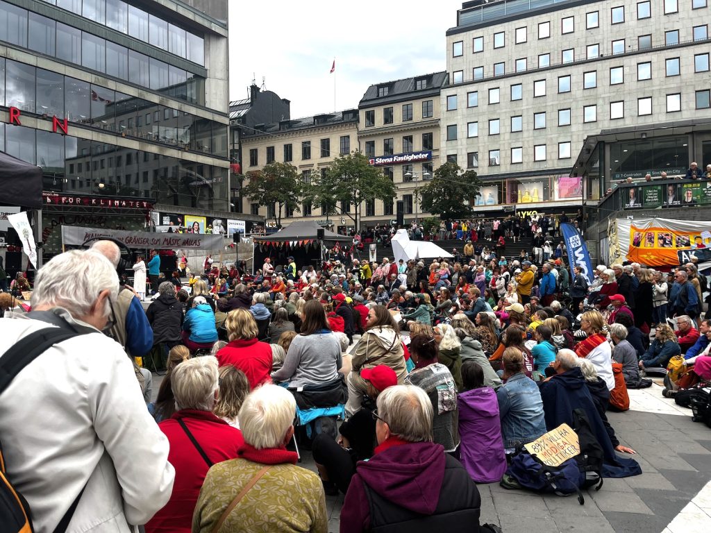 En massa människor sitter framför en scen på Sergels torg.