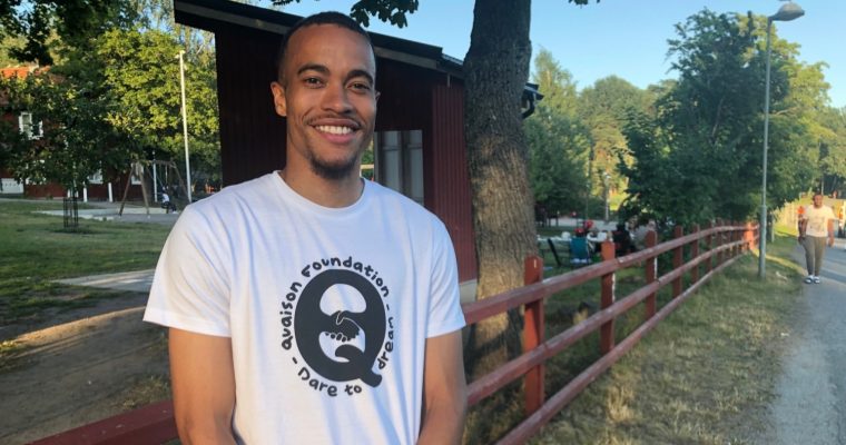 En man i t-shirt står framför ett staket.